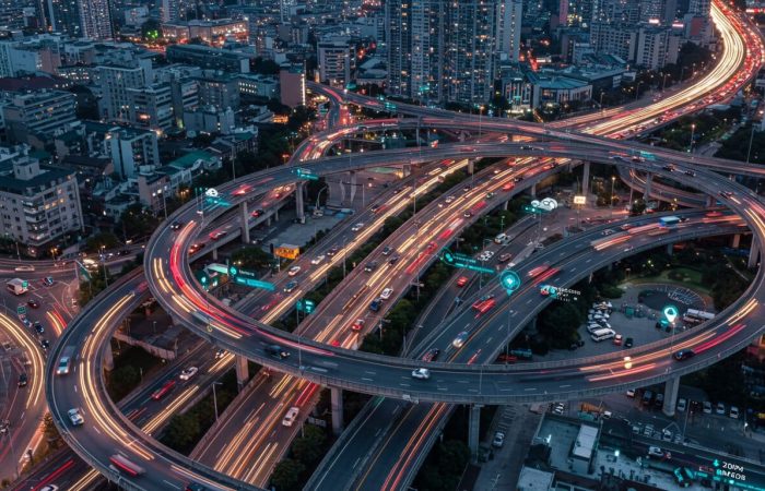 Futuristic urban roads with self-driving and regular cars navigating optimized paths. AI predictive traffic optimization reduces congestion using live traffic, weather, and behavior data.