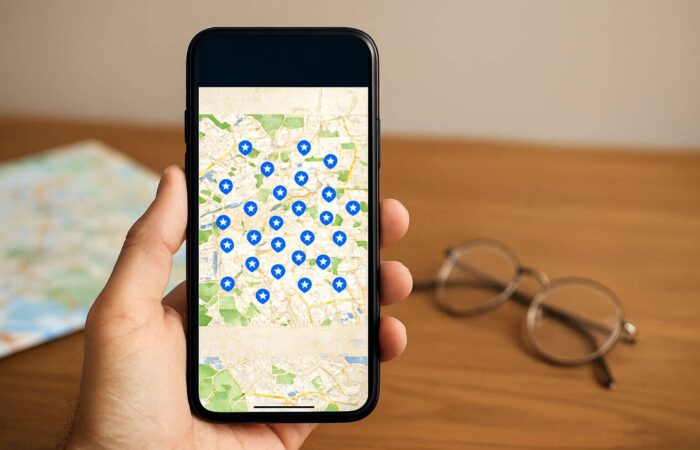 A hand holds a smartphone displaying a map filled with blue markers highlighting Points of Interest(POIs)